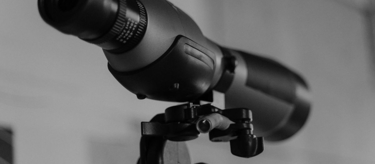 Detailed monochrome image of a modern telescope lens mounted on a tripod.