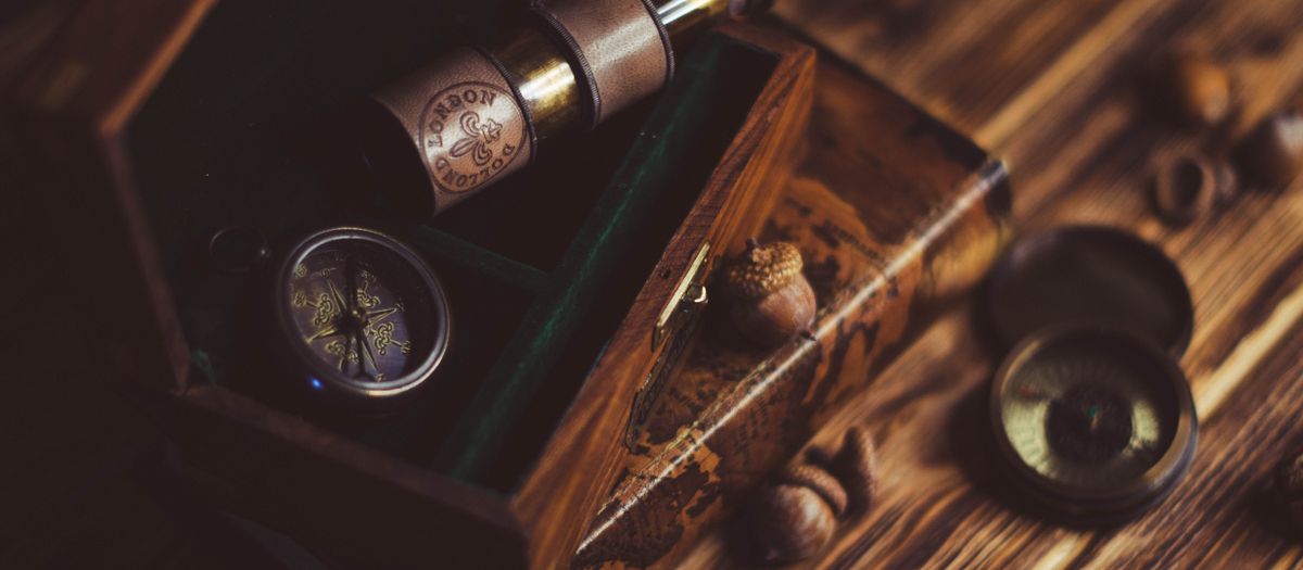 A vintage wooden box containing a telescope and compass on a rustic table.