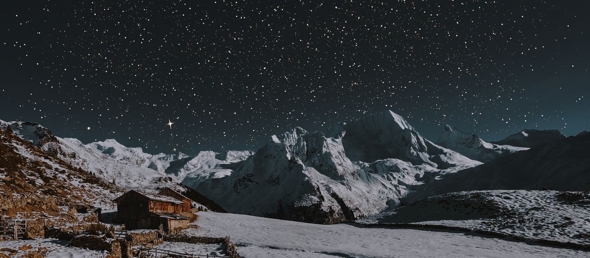 A breathtaking starry night over a snow-capped mountain landscape with a rustic cabin.