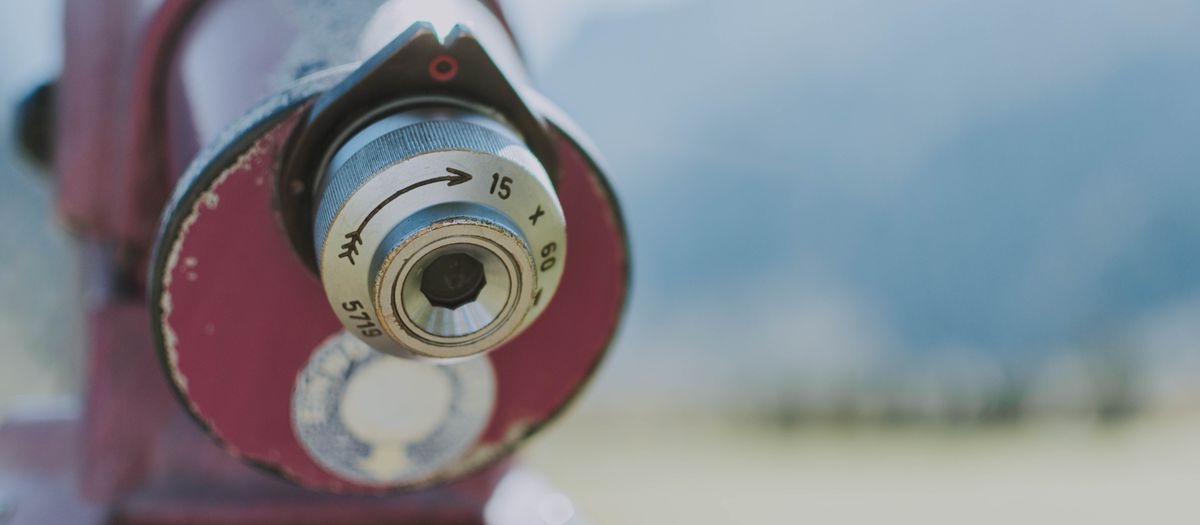 Detailed close-up of an outdoor telescope lens with a blurred natural background.