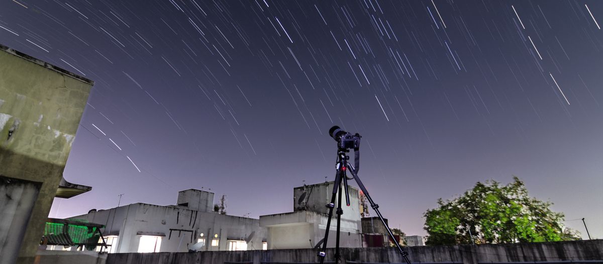 A telescope on a rooftop captures star trails in the night sky.